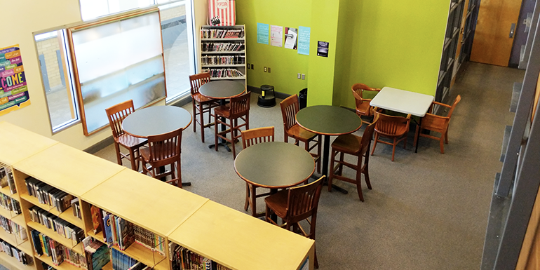 Image of the teen department of Cornwall Public Library including lime green walls, circular tables, book stacks, and various chairs